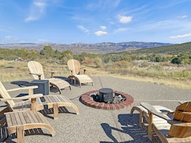 An outdoor seating area with Adirondack chairs and a fire pit, overlooking a mountainous landscape.