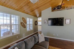 A living room with a wooden ceiling, a gray sofa, a flat-screen TV, and a large window.