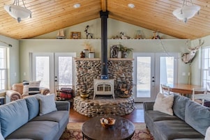 A cozy living room with a stone fireplace, wooden ceiling, and comfortable seating.