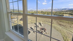 Ein Zimmer mit großem Fenster und Blick auf eine Terrasse mit Gartenmöbeln sowie eine malerische Aussicht auf Berge und Bäume.