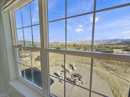 A room with a large window overlooking a patio with outdoor furniture and a scenic view of mountains and trees.