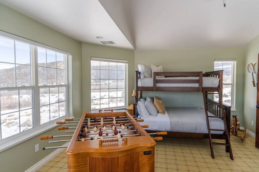A room with a foosball table, bunk beds, and large windows offering a view of a snowy landscape.
