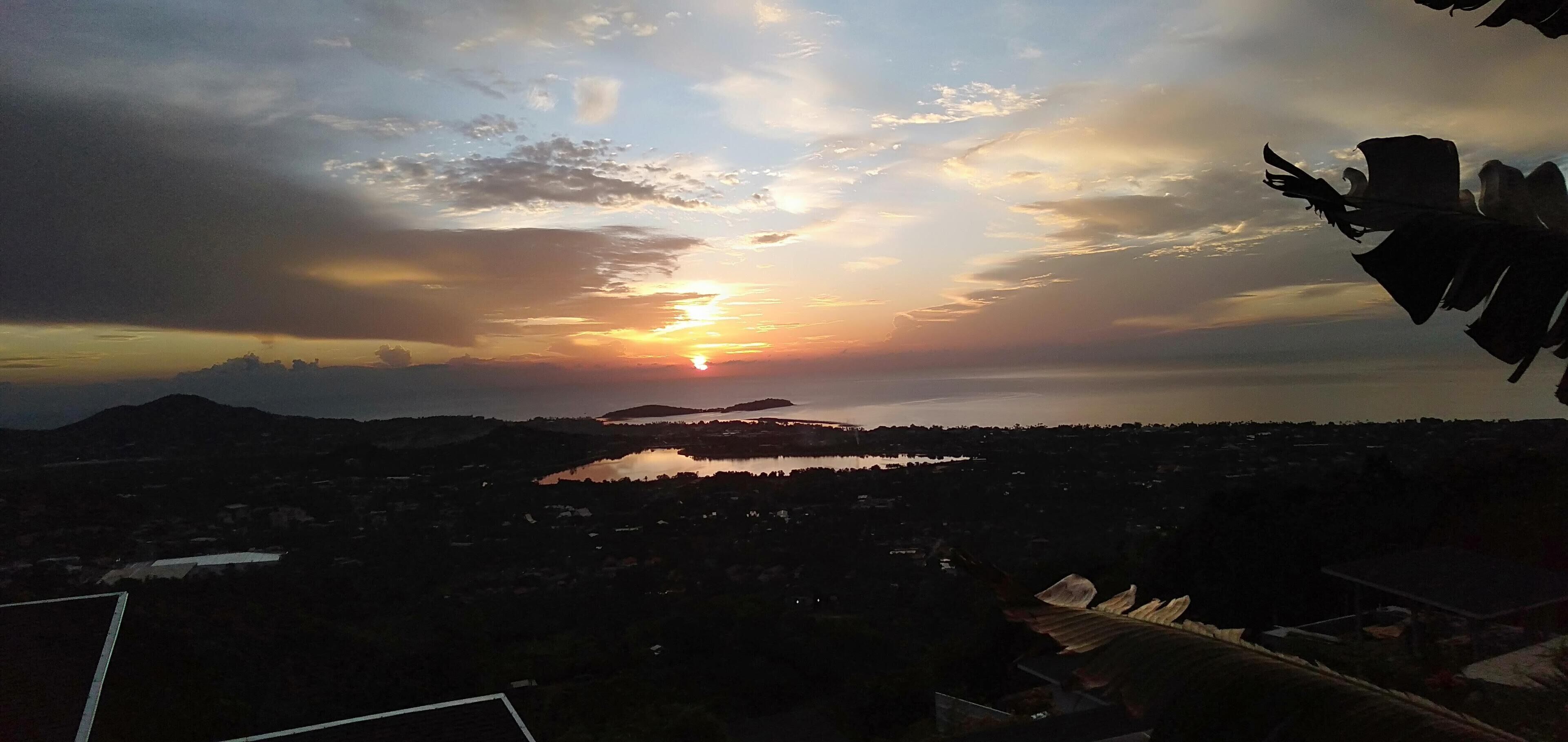 A sunset over a lake with surrounding hills and a distant cityscape.