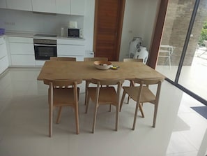 A modern kitchen with white cabinets, a microwave, and an oven. There is a wooden dining table with four chairs. - Great Sea view Mountain Villa (Koh Samui)