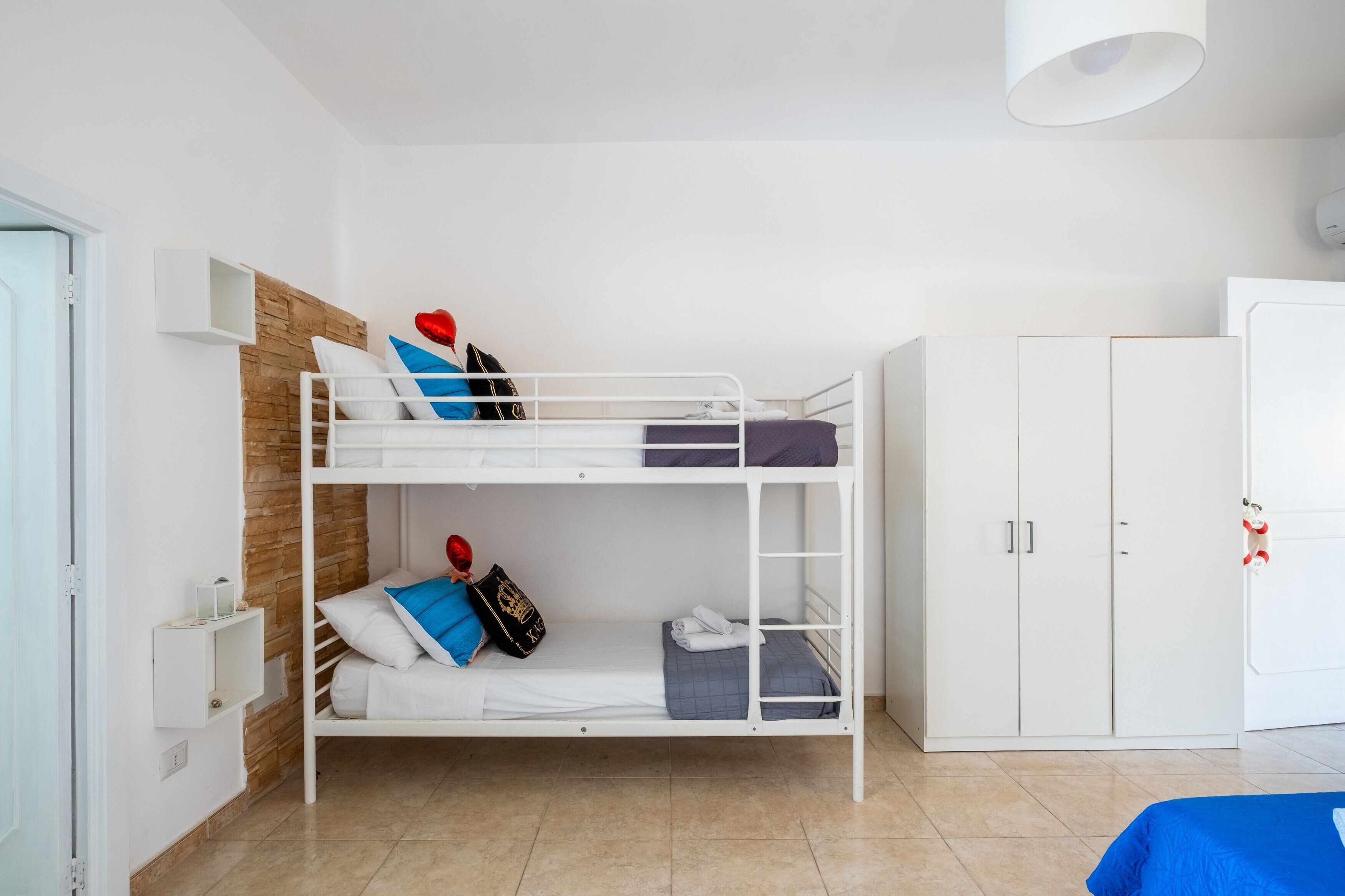A bunk bed with white bedding, a wooden headboard, a white wardrobe, and a white door.