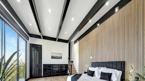 Un dormitorio moderno con una cama grande, piso de madera, cabecera negra y vista al exterior.