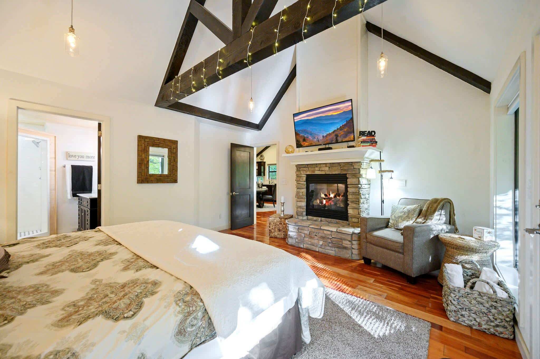 A spacious bedroom with a large bed, a fireplace, a television, and a cozy seating area.