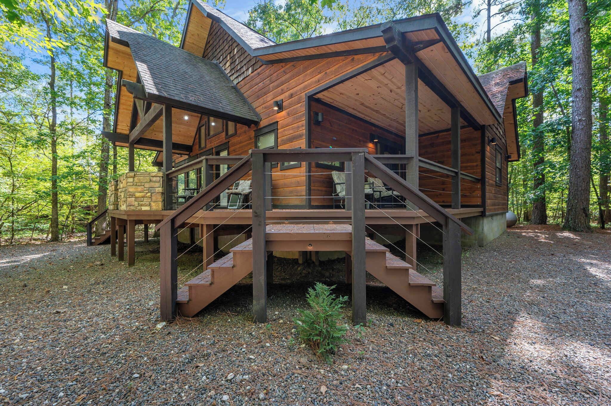 Une cabane avec une façade en bois, des fondations en pierre et une terrasse en bois avec un escalier menant à l’entrée.