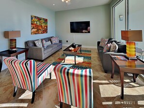 A modern living room with a grey sofa, striped chairs, a coffee table, and a TV on the wall.
