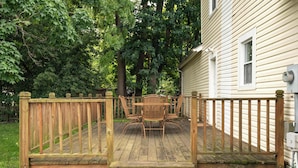 A wooden deck with a table and chairs, surrounded by a wooden fence, and a house in the background.
