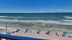 A beachside view with a pool area, lounge chairs, and umbrellas. - Harbour Beach Resort 503 | Oceanfront + Amenities (Daytona Beach)