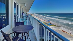 Un balcon avec une table et des chaises, donnant sur une plage, avec une rambarde et un poste de surveillance pour les sauveteurs.