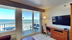 Una stanza con una grande TV, una scrivania in legno, una sedia e vista sull'oceano.