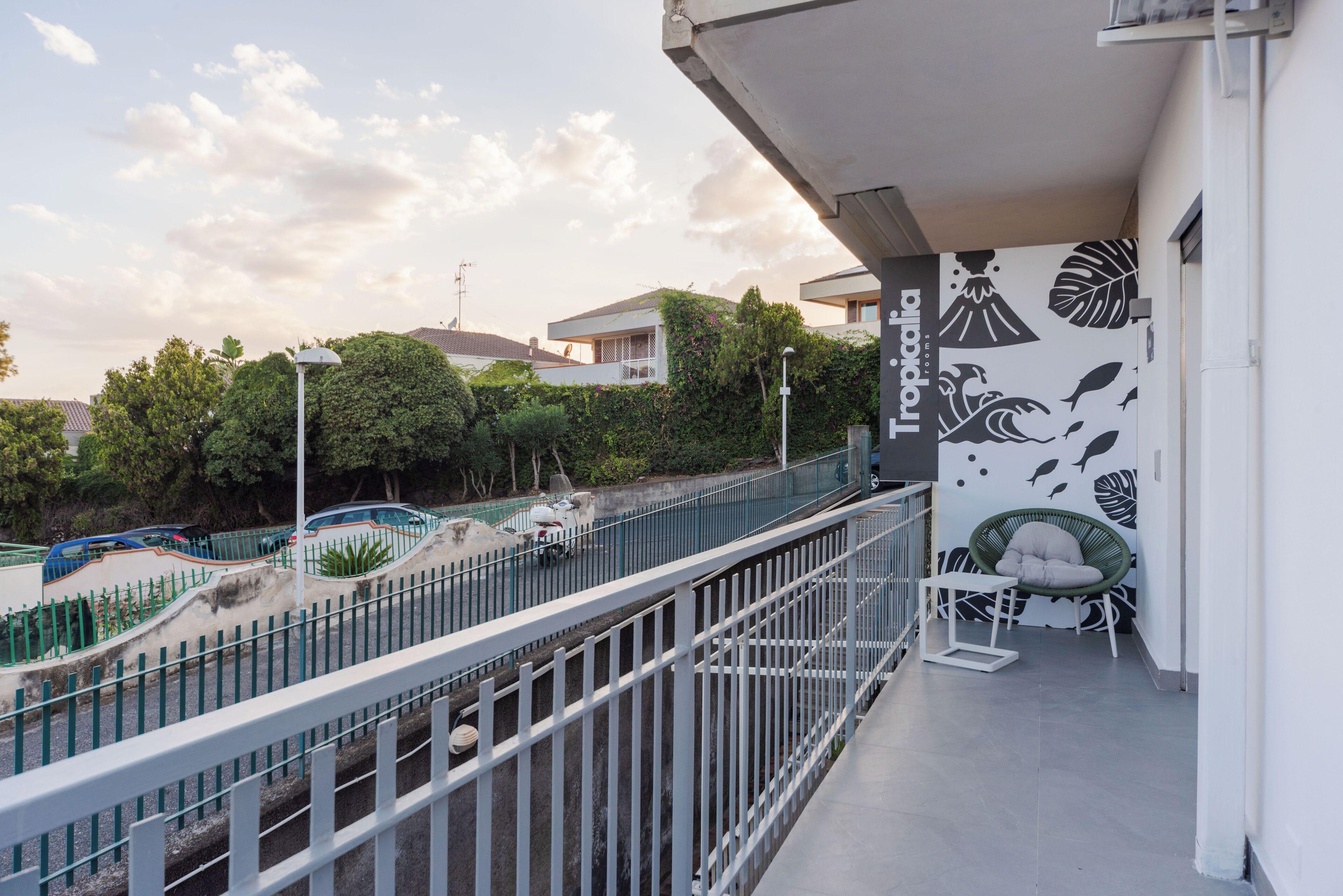 A balcony with a white railing, a chair, and a table. There is a wall with a tropical leaf pattern.