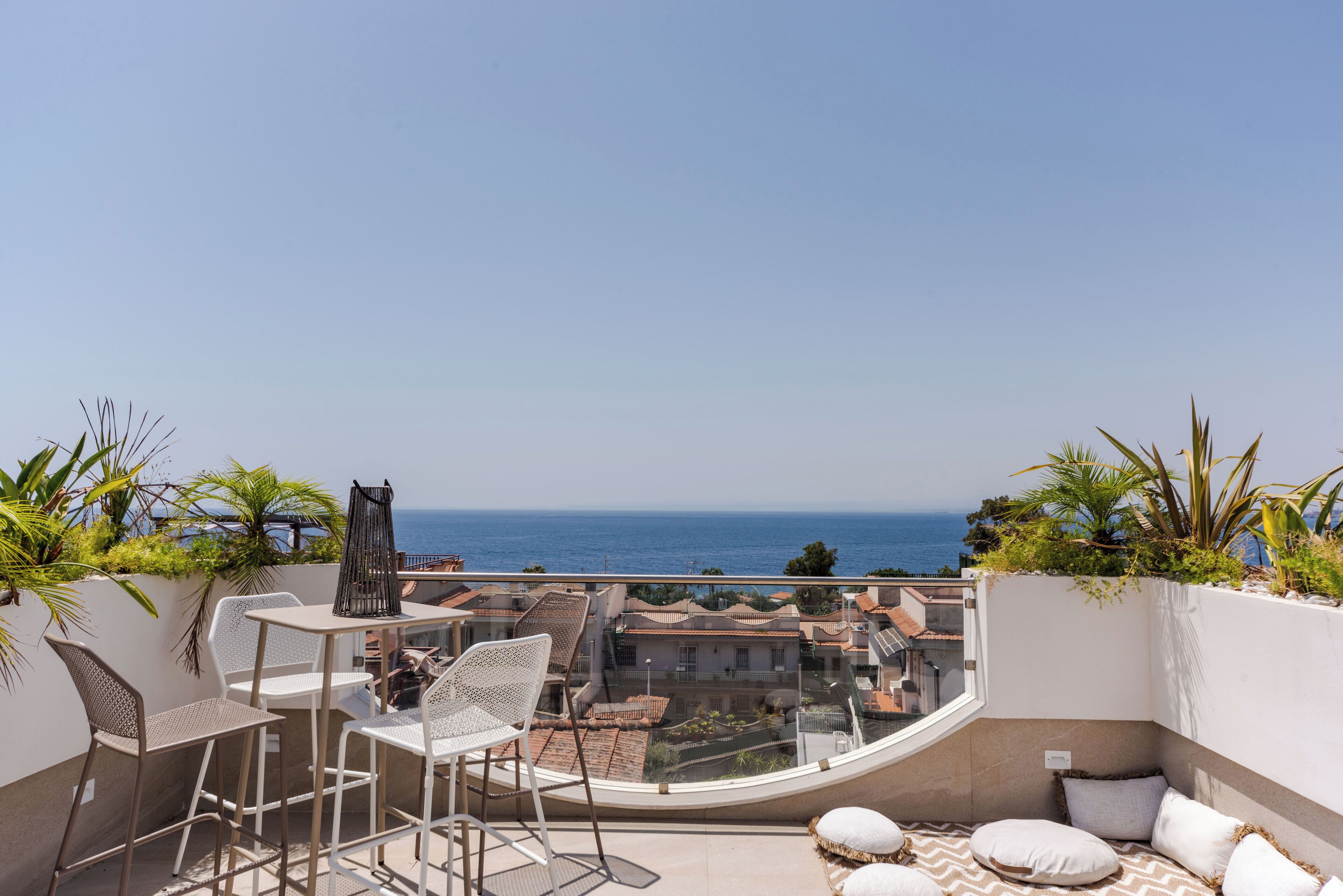 A balcony with a table and chairs, a sofa, and a view of the sea and buildings.