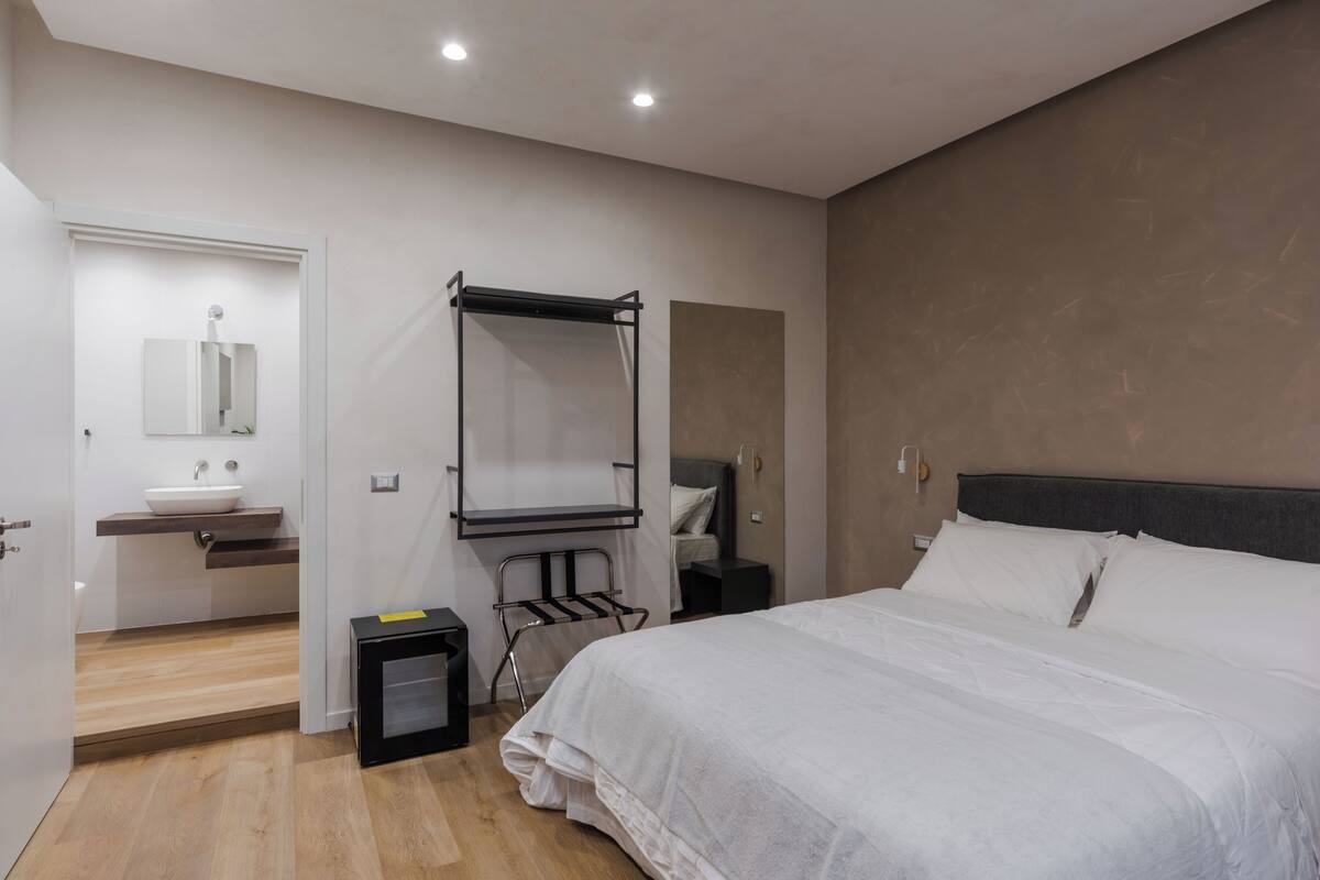 Quarto de hotel moderno com uma cama grande, pia embutida, espelho e uma mesa pequena.
