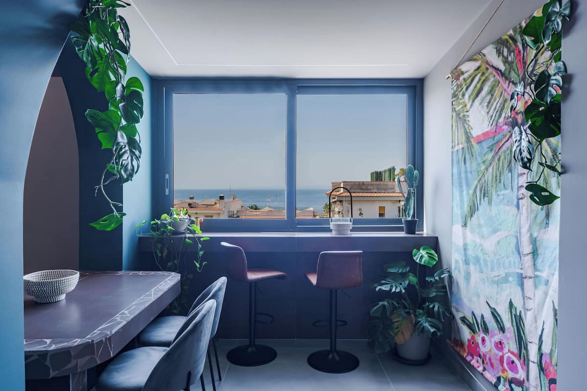 Uma varanda com vista para o mar, uma mesa com cadeiras e plantas em vasos.