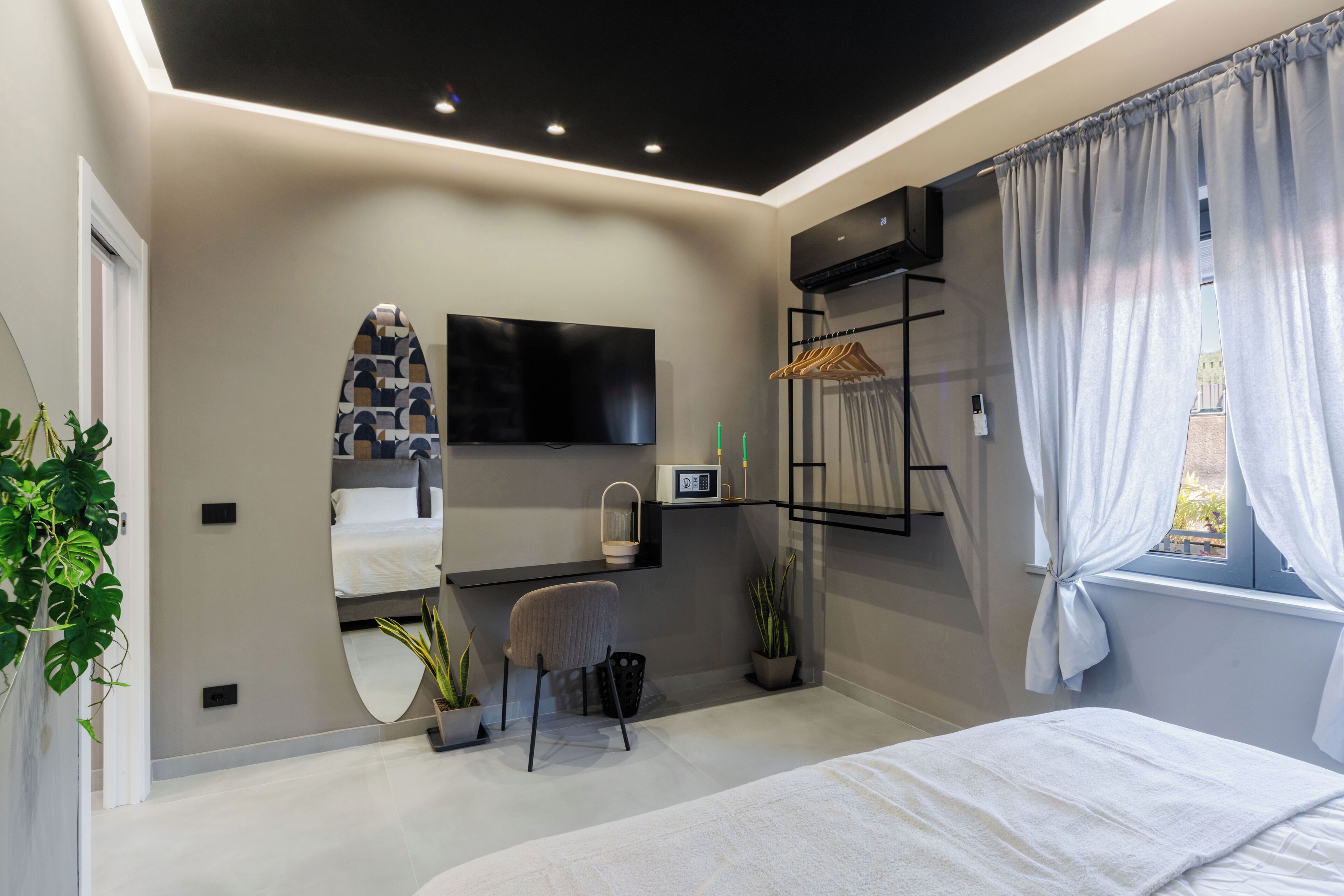 A modern bedroom with a bed, a desk, a chair, a TV, and a window with curtains.