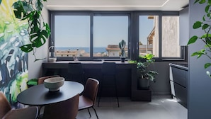 A modern kitchen with a large window, a dining area with chairs and a table, and a potted plant. - Tropicalia Suites by Wonderful Italy  (Aci Castello)