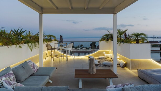 A covered outdoor seating area with a sofa, chairs, and a table, overlooking a body of water. - Tropicalia Suites by Wonderful Italy  (Aci Castello)
