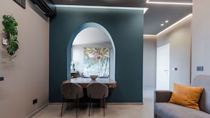 A modern living room with a dining area, featuring a sofa, a table with chairs, and a large window with a tropical view. - Tropicalia Suites by Wonderful Italy  (Aci Castello)