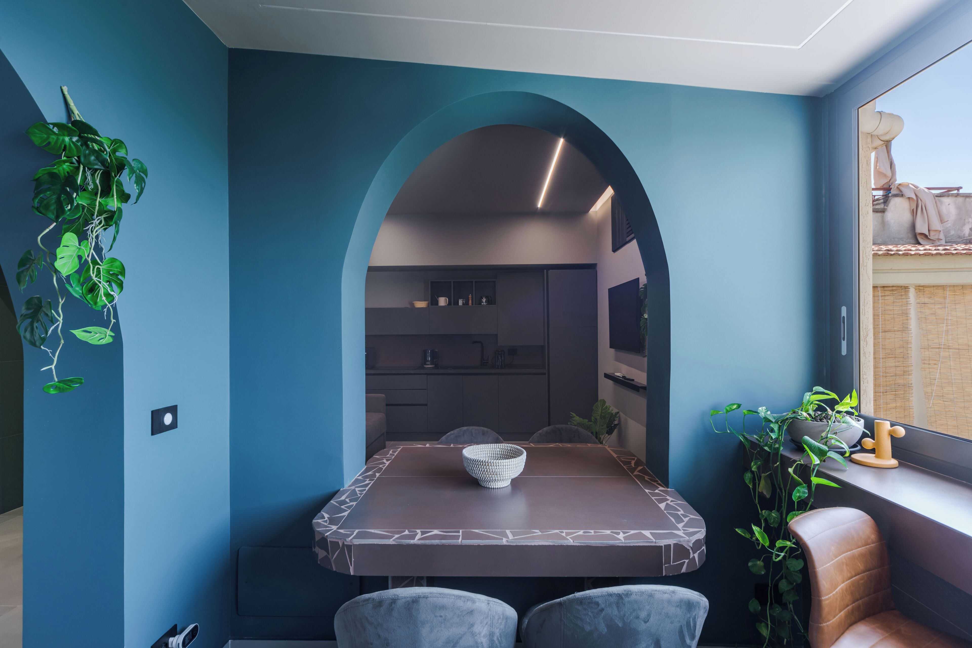A dining area with a table and chairs, a plant on the wall, and a view into the kitchen.