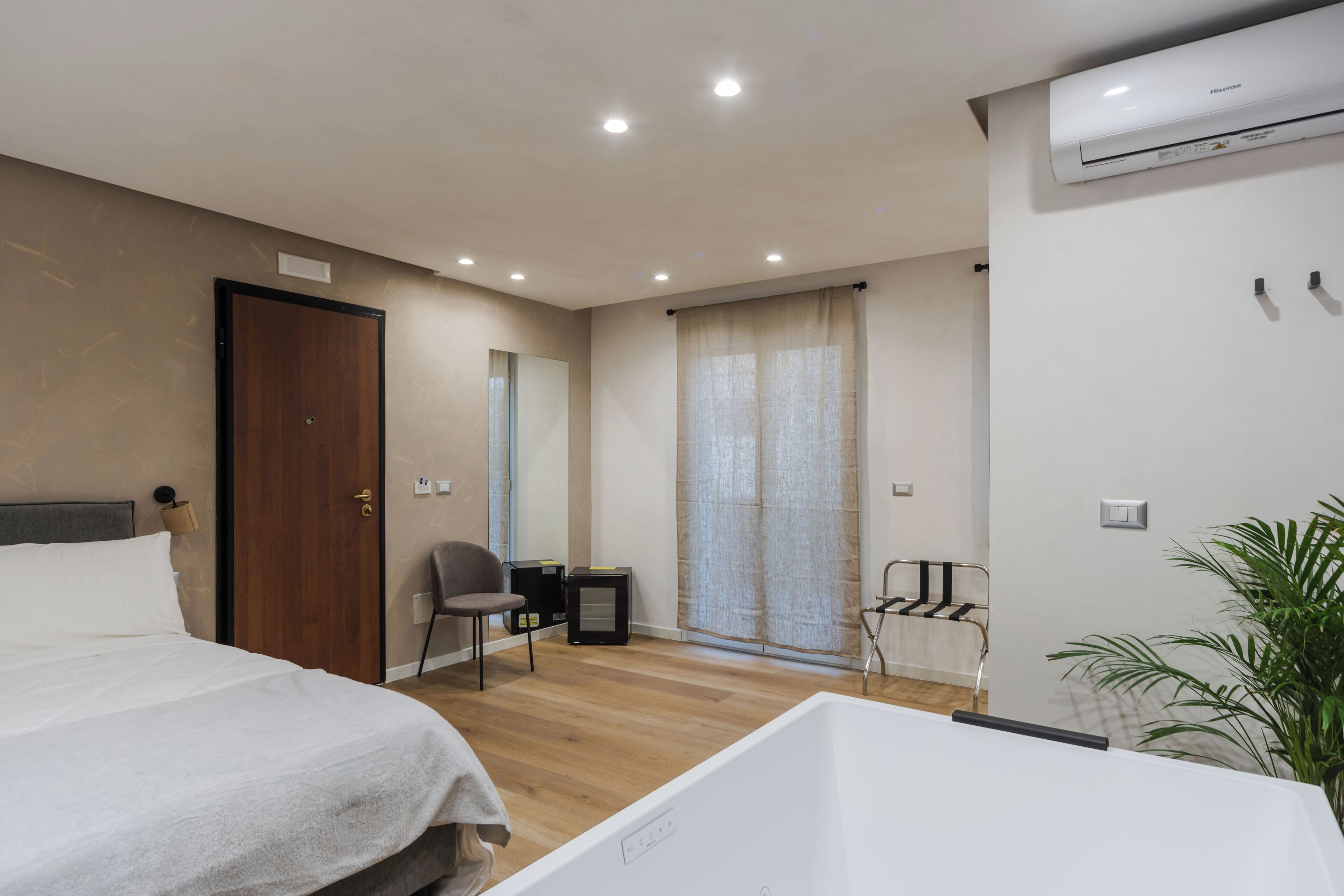 Ein modernes Hotelzimmer mit einem großen Bett, einem kleineren Bett, einem Schreibtisch, einem Stuhl, einem Fenster mit Vorhängen und einer Klimaanlage.