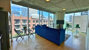A spacious room with large windows, a blue sofa, a small table, and a TV.