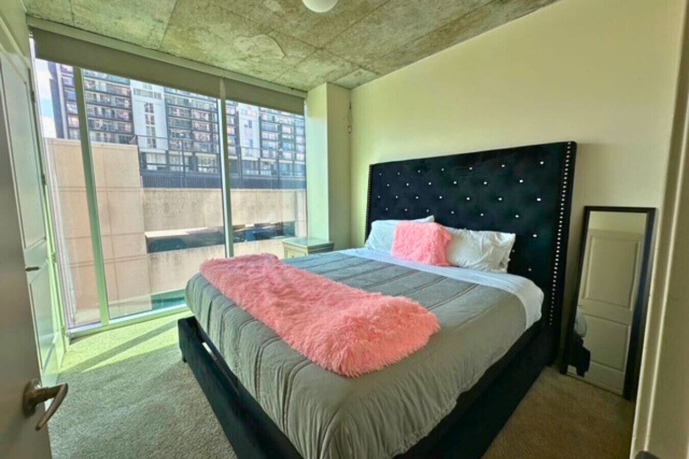 Ein Schlafzimmer mit einem großen Bett, einem schwarzen Kopfteil und einer rosa Tagesdecke.