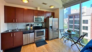 A modern kitchen with stainless steel appliances, wooden cabinets, and a dining area with a view of the city.