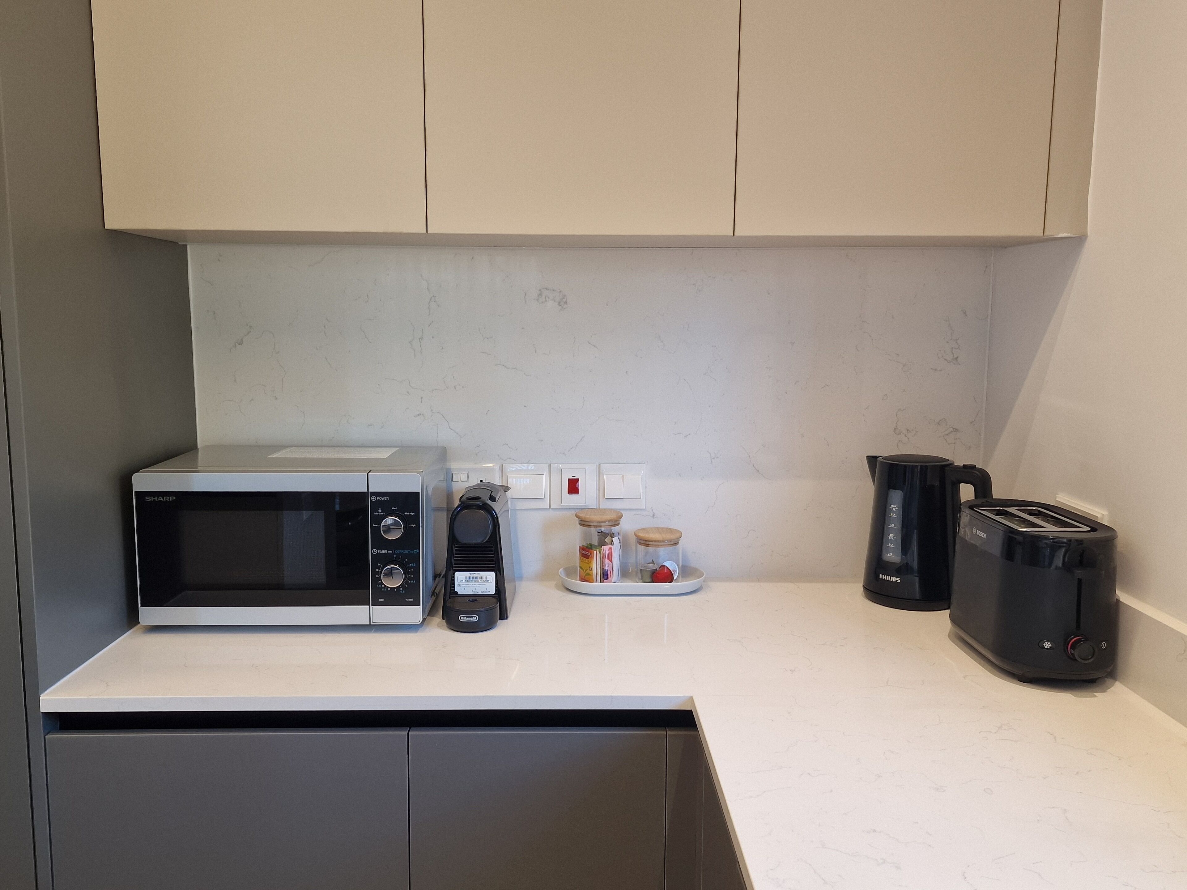 A kitchen with a microwave, coffee maker, toaster, and cabinets.