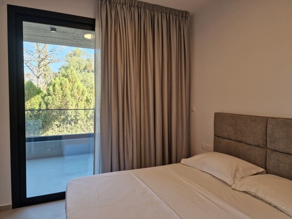 A bedroom with a large window, a balcony, and a bed with white bedding. - Hypnos Park View (Strovolos)