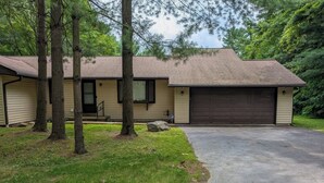 A single-story house with a garage, surrounded by trees and a grassy yard. - The Pines at New Albany | Sleeps 8 | Acre Lot (New Albany)