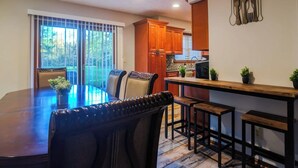 A dining area with a large table and chairs, a kitchen with wooden cabinets, and a view through the glass door. - The Pines at New Albany | Sleeps 8 | Acre Lot (New Albany)
