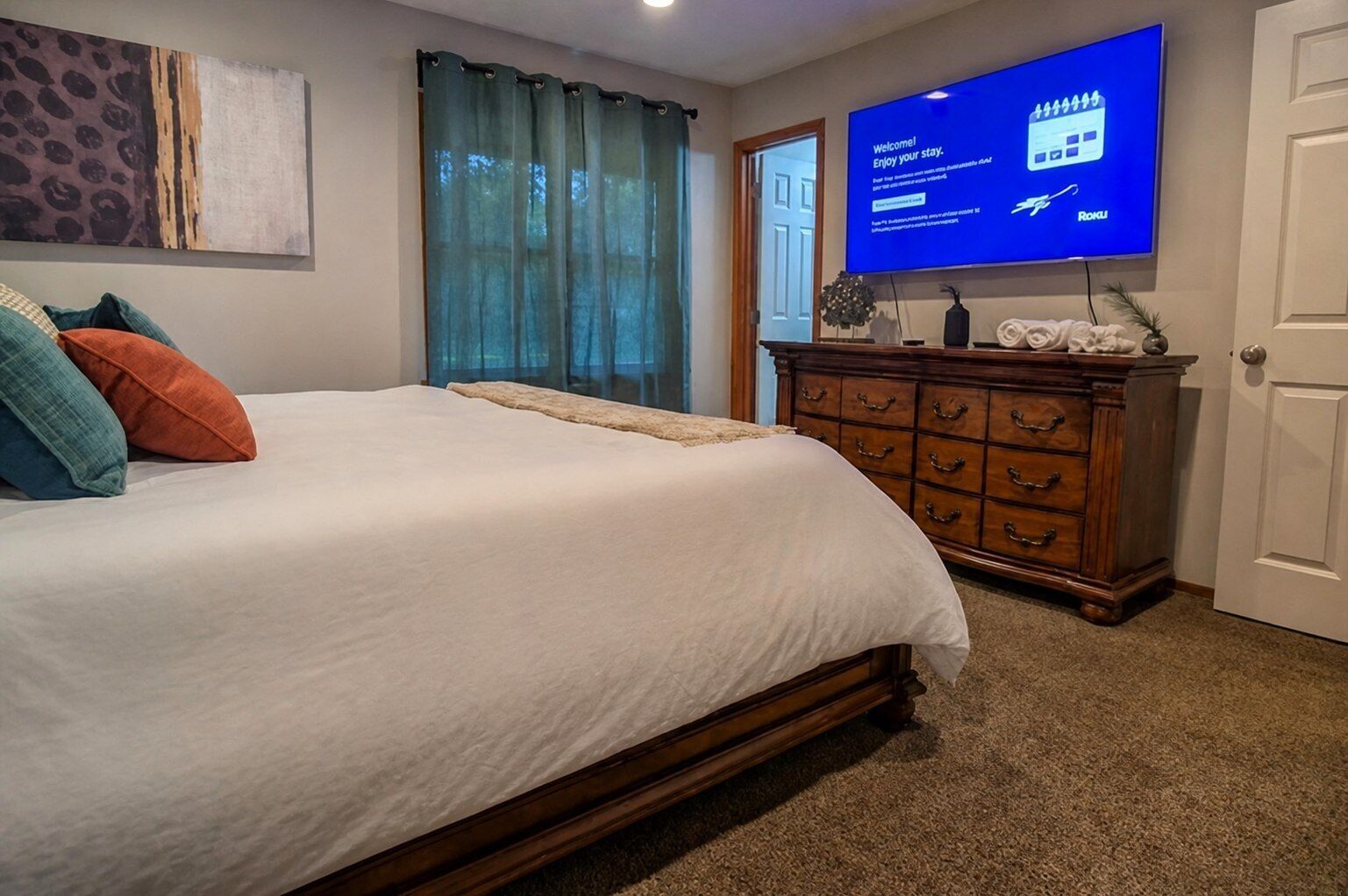 A bedroom with a bed, a dresser, a television displaying a welcome message, and a door.