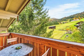 A wooden deck with a table and chairs, overlooking a green landscape with houses and trees.