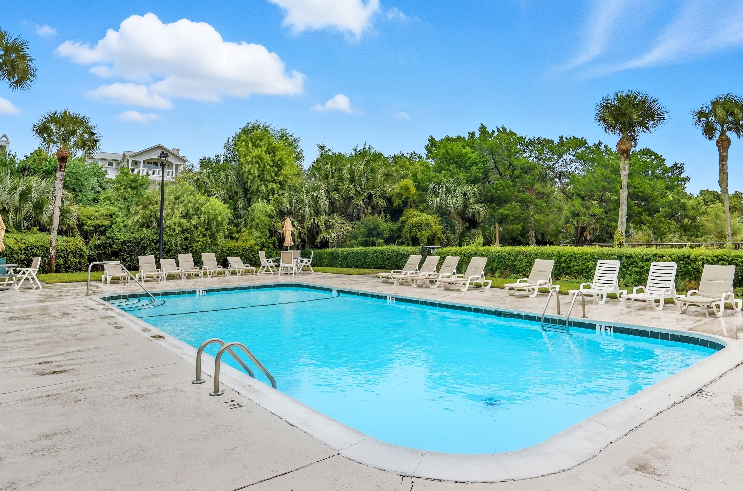 A rectangular swimming pool with a 7 FT depth marker, surrounded by lounge chairs and palm trees.