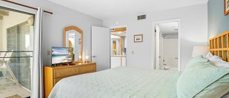 A bedroom with a bed, a dresser, a television, and a sliding glass door leading to a balcony.