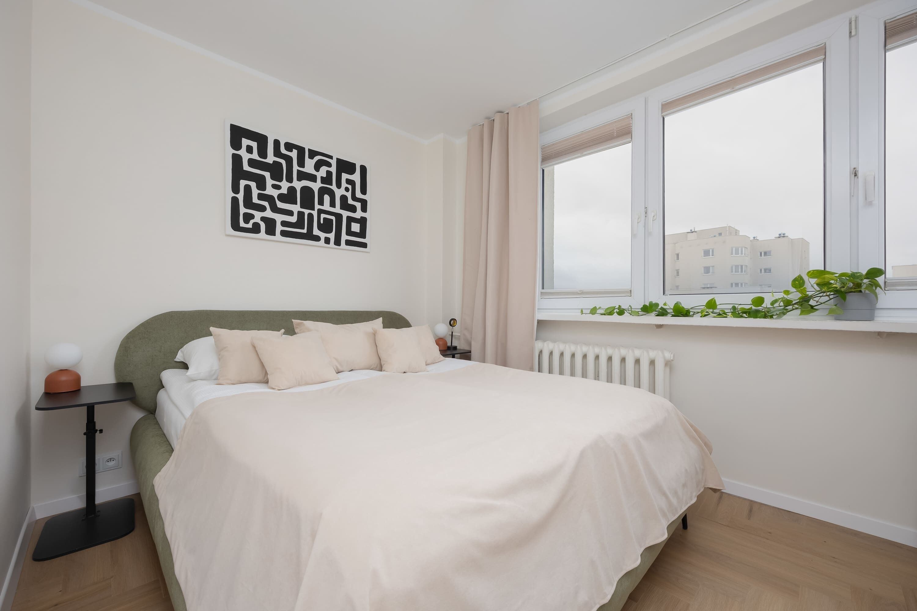 Una camera da letto con un letto, un comodino, un termosifone e una finestra vista edifici.