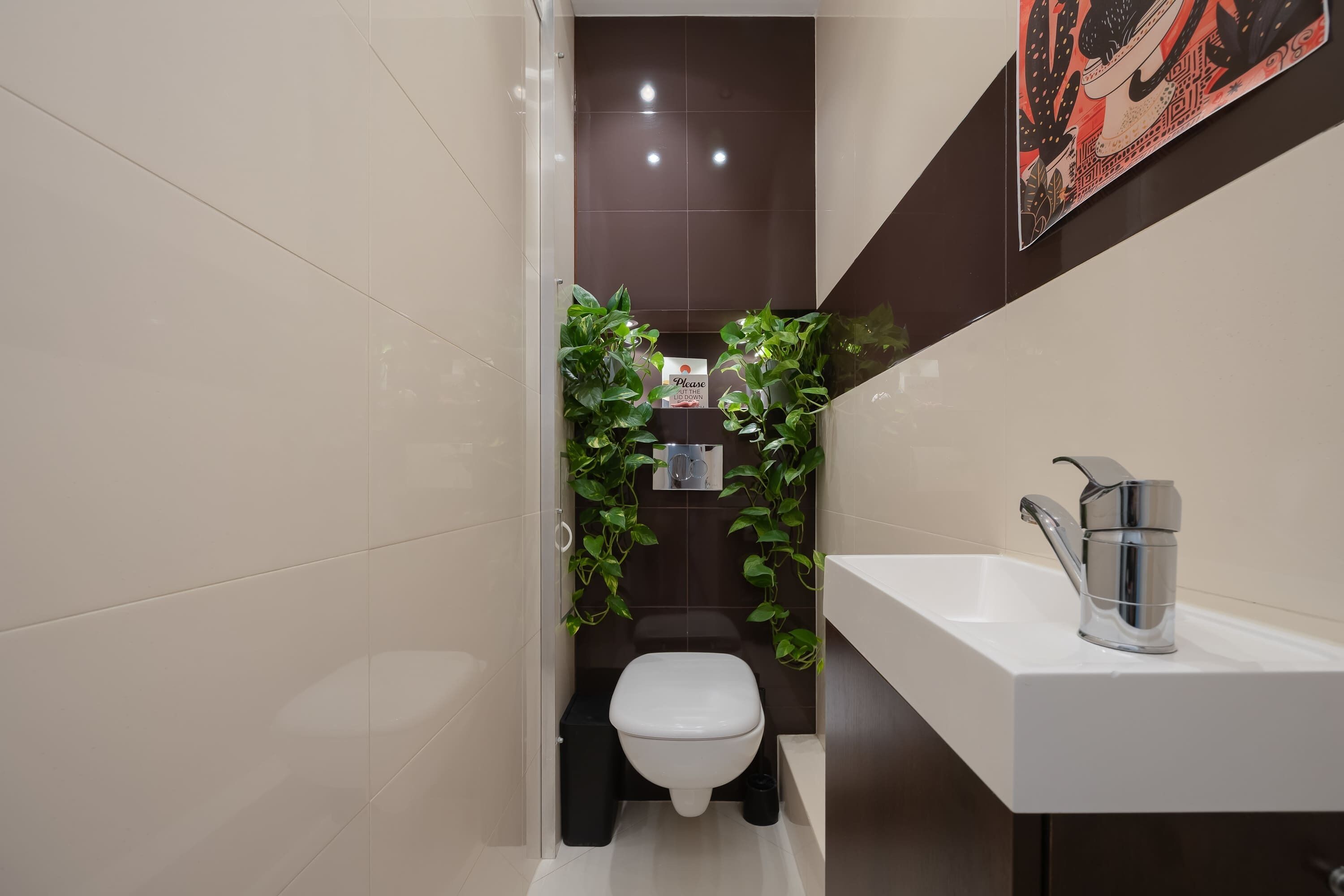 A modern bathroom with a white toilet, a sink with a chrome faucet, and decorative plants.