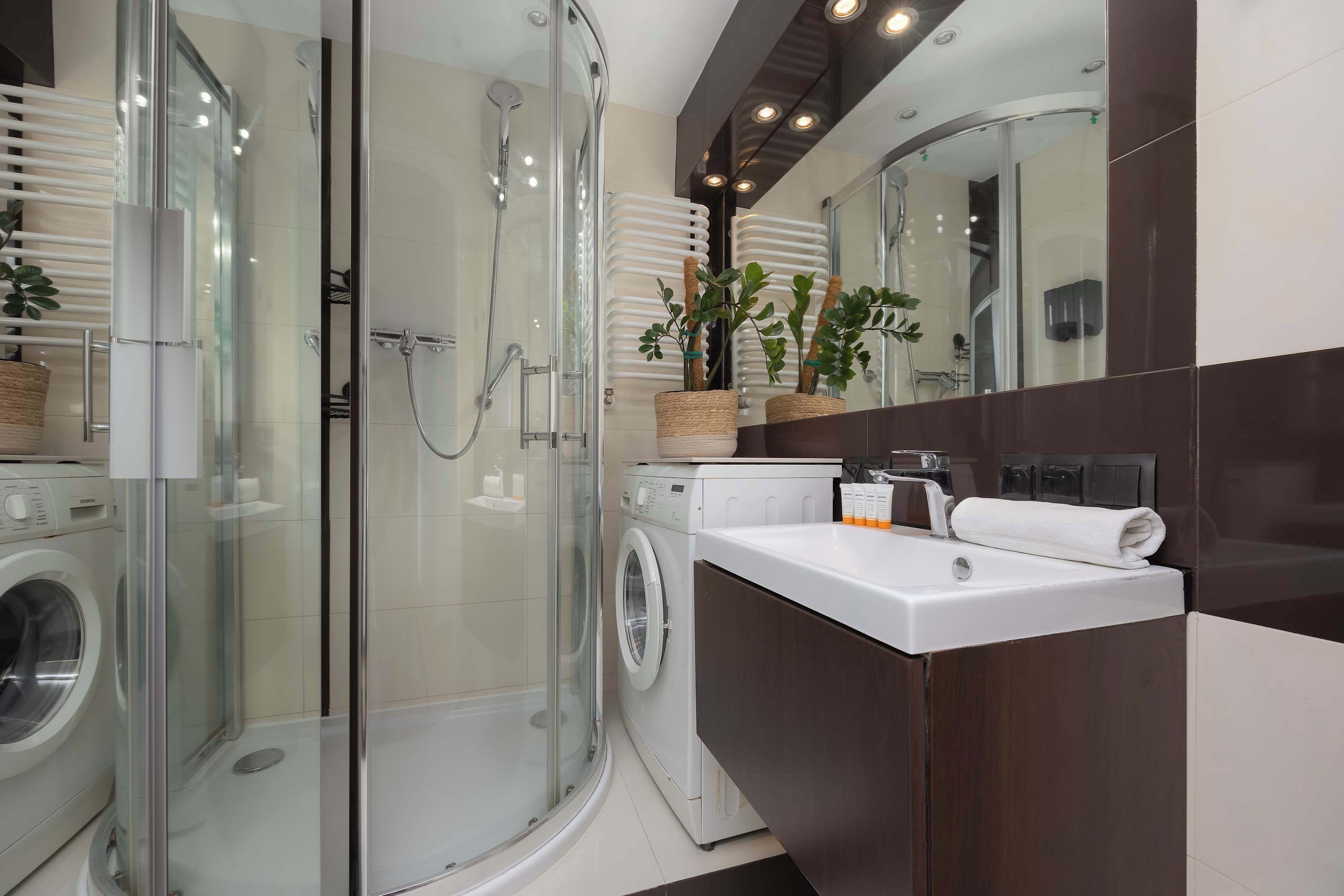 Un baño moderno con ducha de vidrio, lavadora e lavabo con espejo.