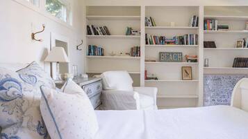 A bedroom with a bed, a chair, a nightstand, a lamp, and a bookshelf filled with books.