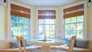 A bay window seating area with a round glass table, cushioned chairs, and a vase on the table. - Waterfront Saunderstown Estate with Private Dock (North Kingstown)