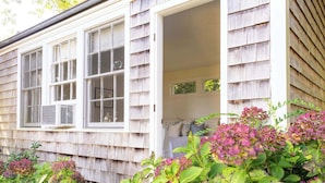 A wooden house with a porch, large windows, and a garden with hydrangeas. - Waterfront Saunderstown Estate with Private Dock (North Kingstown)
