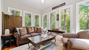 A cozy living room with a brown leather sofa, a wooden coffee table, and large windows offering a view of the trees. - Cozy Mountain Getaway in Big Canoe (Big Canoe)