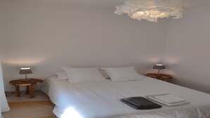 Un lit bien fait, avec du linge de lit blanc, deux tables de chevet avec des lampes et un lustre moderne.