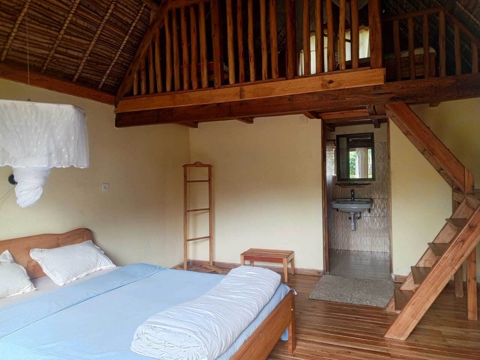 Quarto com cama, escada de madeira, uma mesinha, escada e banheiro com pia.