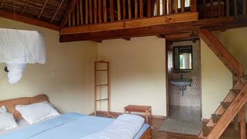 Quarto com cama, escada de madeira, uma mesinha, escada e banheiro com pia.