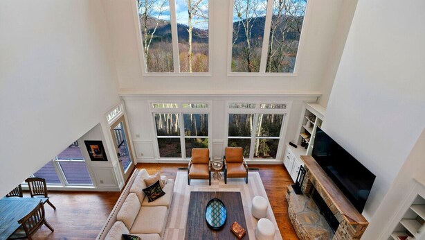 A spacious loft with a high ceiling, large windows offering mountain views, a cozy seating area with a fireplace, and a flat-screen TV mounted on the wall. - Thrush Turn Manor in Big Canoe with a hot tub (Jasper)