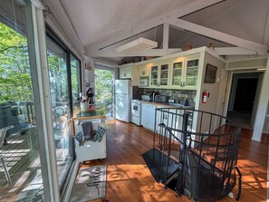 Una cocina moderna con vistas al exterior, un comedor con puerta de vidrio y una escalera con barandilla metálica.